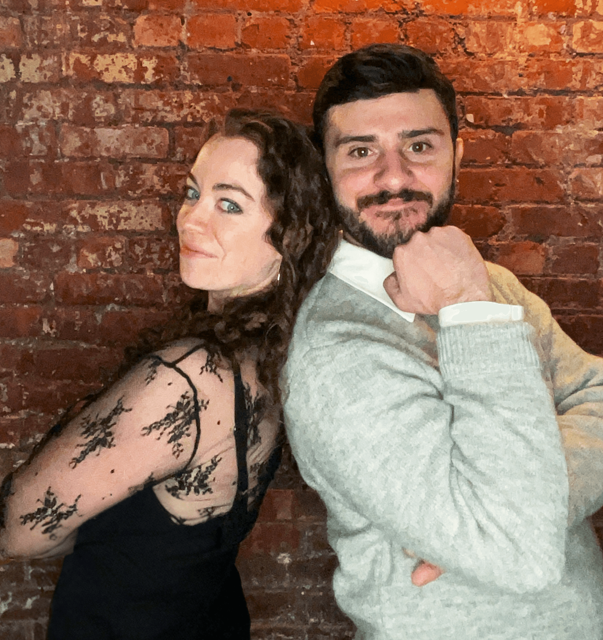 Two people posed back to back in front of a brick wall at a company event