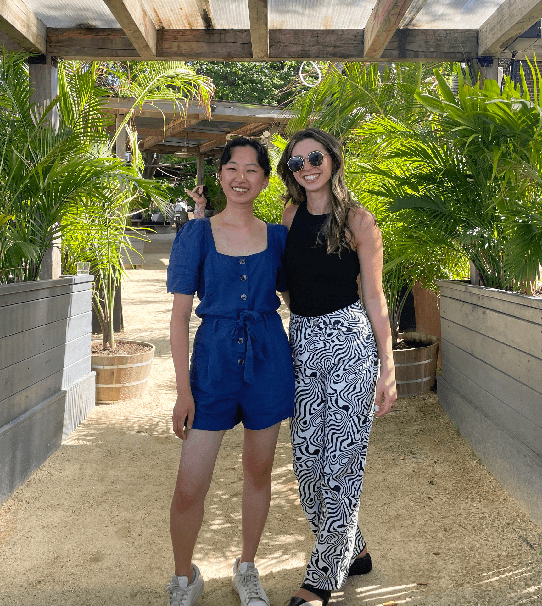 Two women standing together under a pergola smiling for a photo